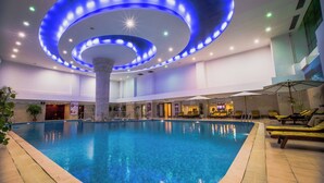Una piscina interior con una columna central, sillas de descanso e iluminación circular en el techo.