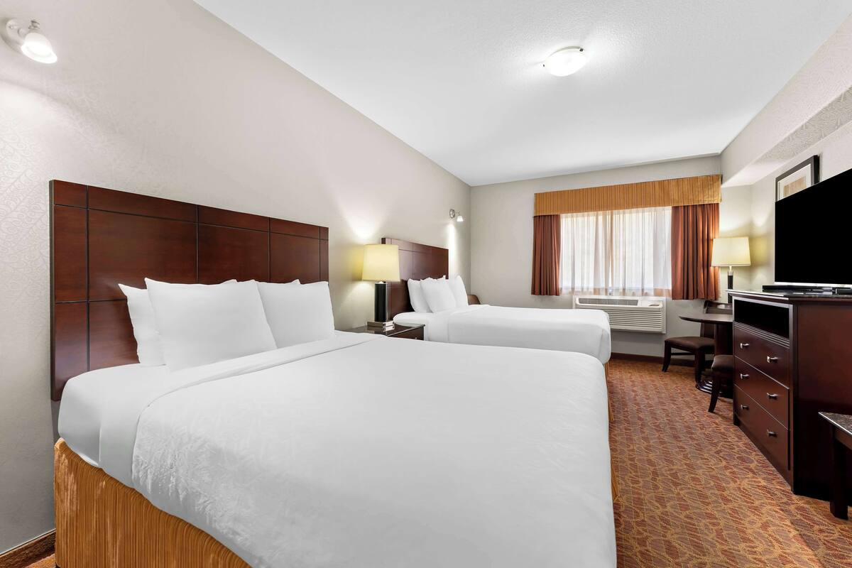 A hotel room with two beds, a desk, a chair, a TV, and a window with curtains.