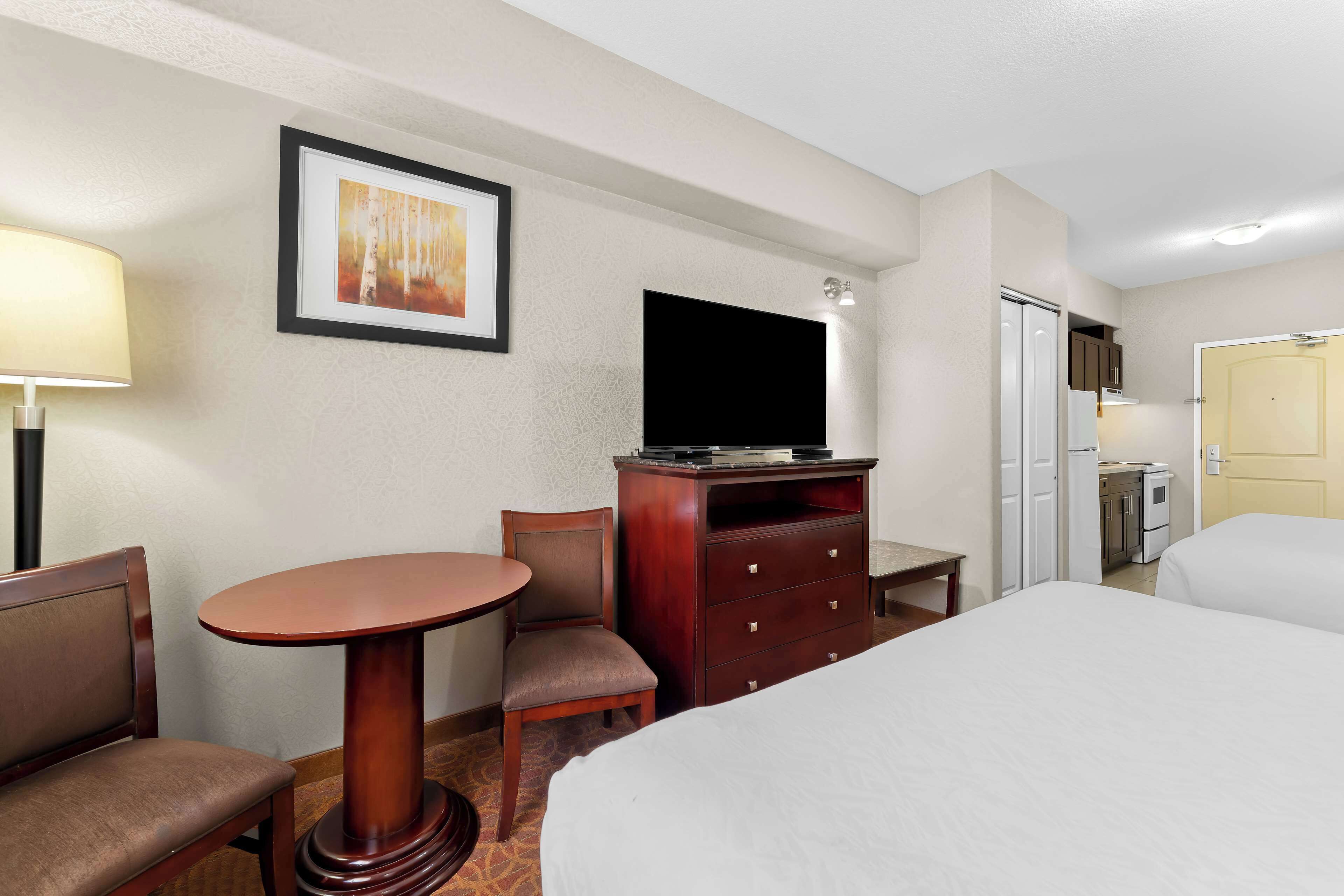 Quarto de hotel com cama, escrivaninha com cadeira, cômoda, televisão e um quadro na parede.