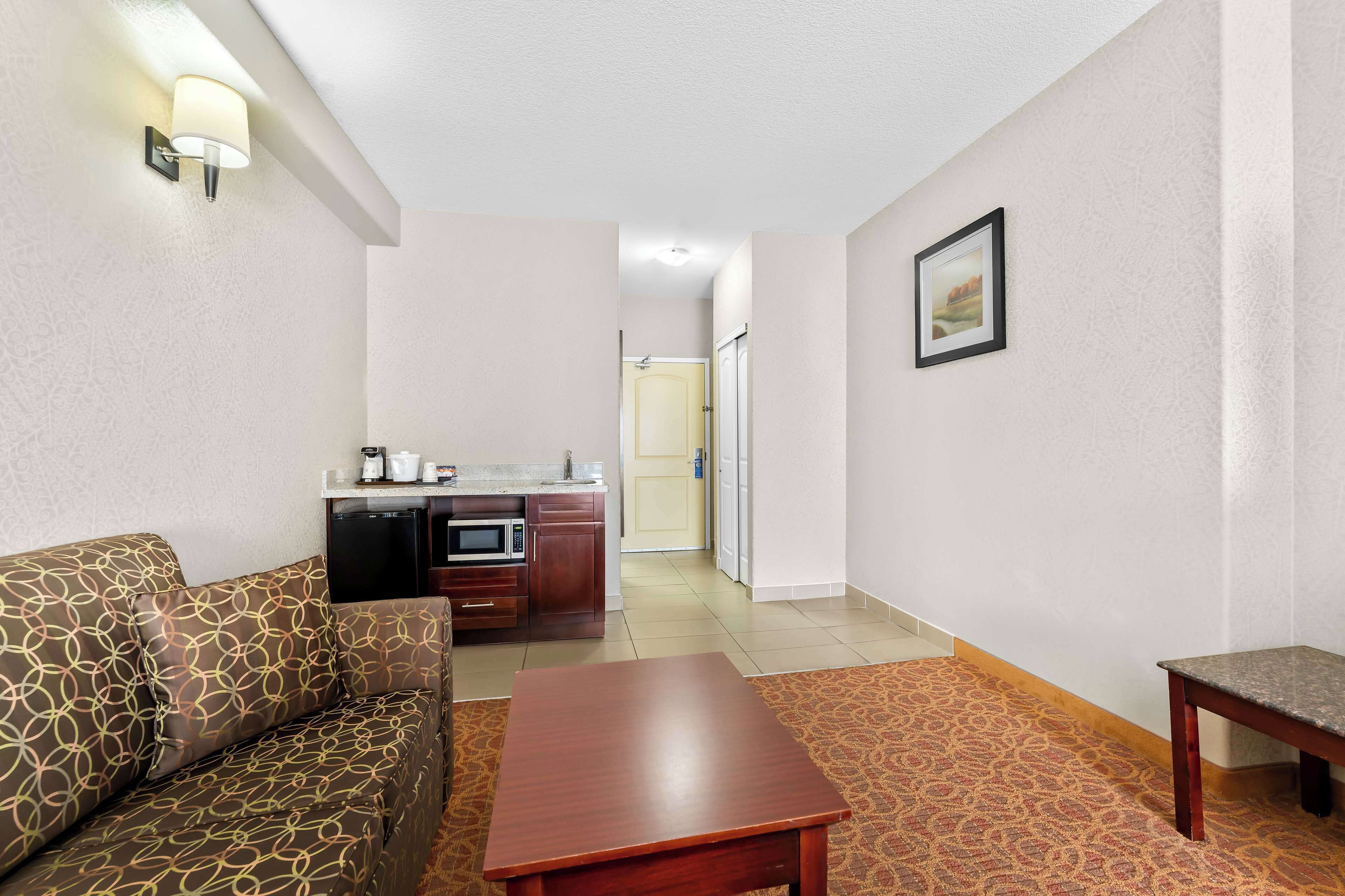 Un espace de vie compact comprenant un canapé, une table en bois, une kitchenette et un tableau encadré au mur.