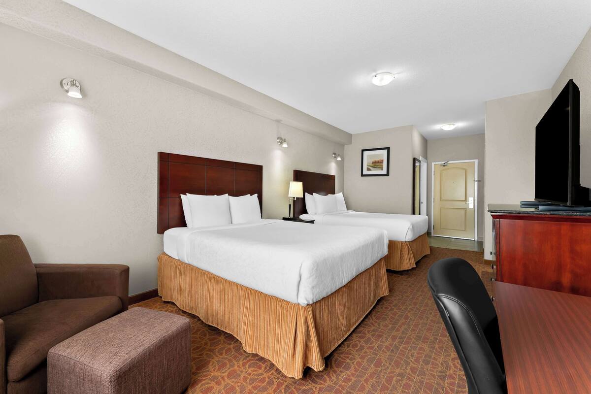 A hotel room with two beds, a desk, a chair, and a television.