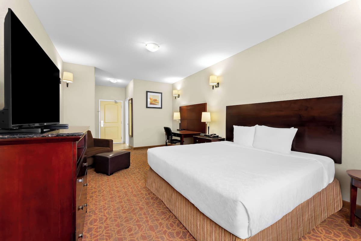 A hotel room with a large bed, a desk, a chair, a television, and a wardrobe.