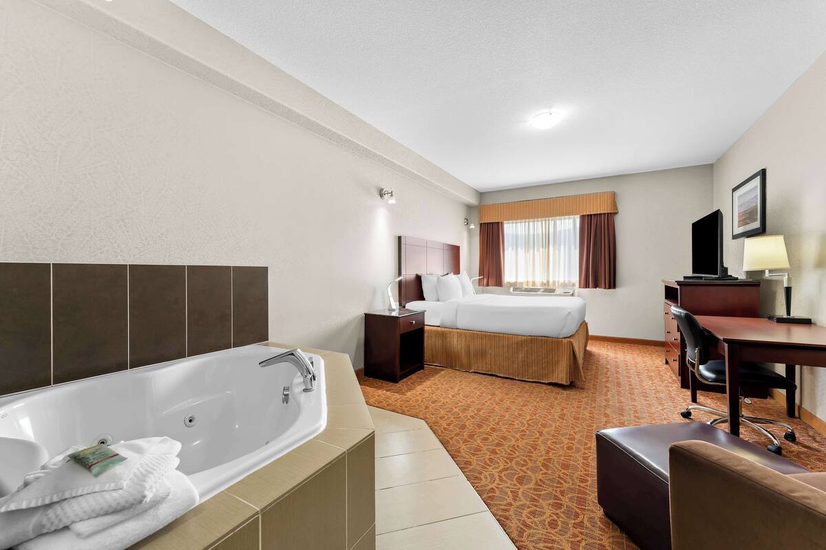 A hotel room with a large bathtub, a bed, a desk with a chair, and a television.