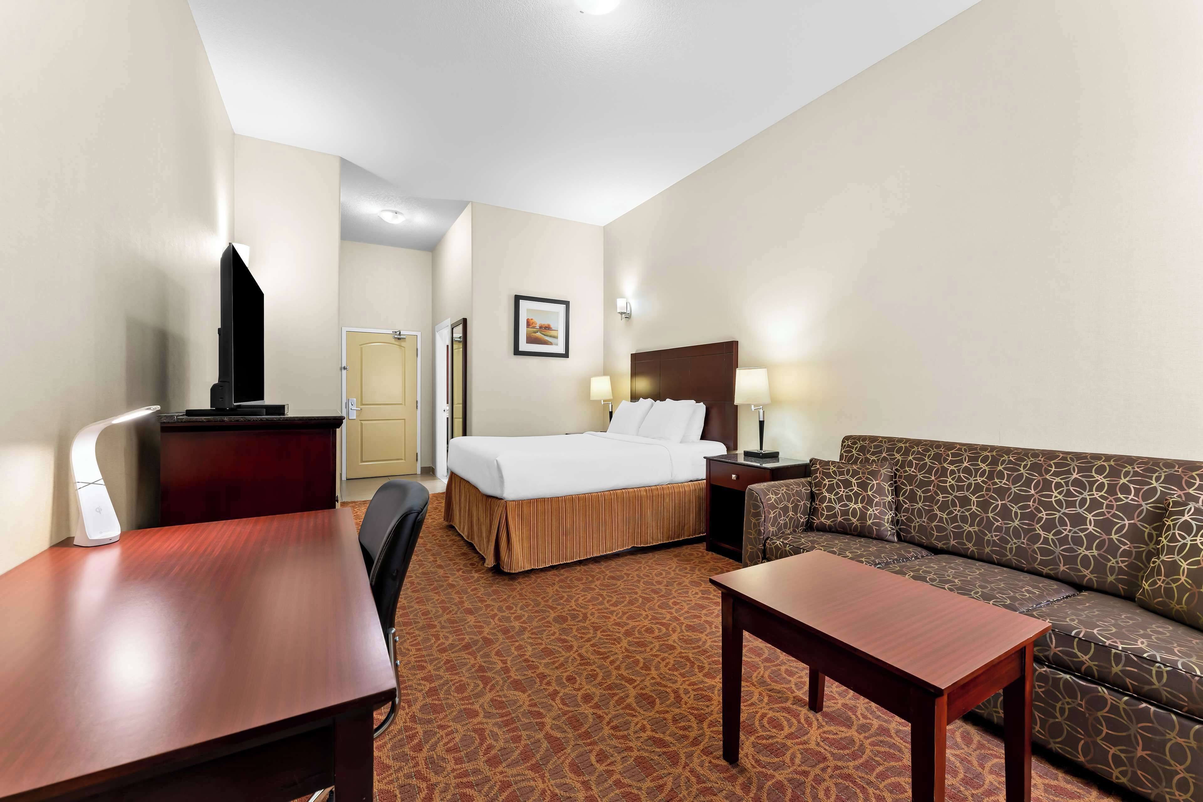 Habitación de hotel con cama, escritorio, silla, sofá y televisor.