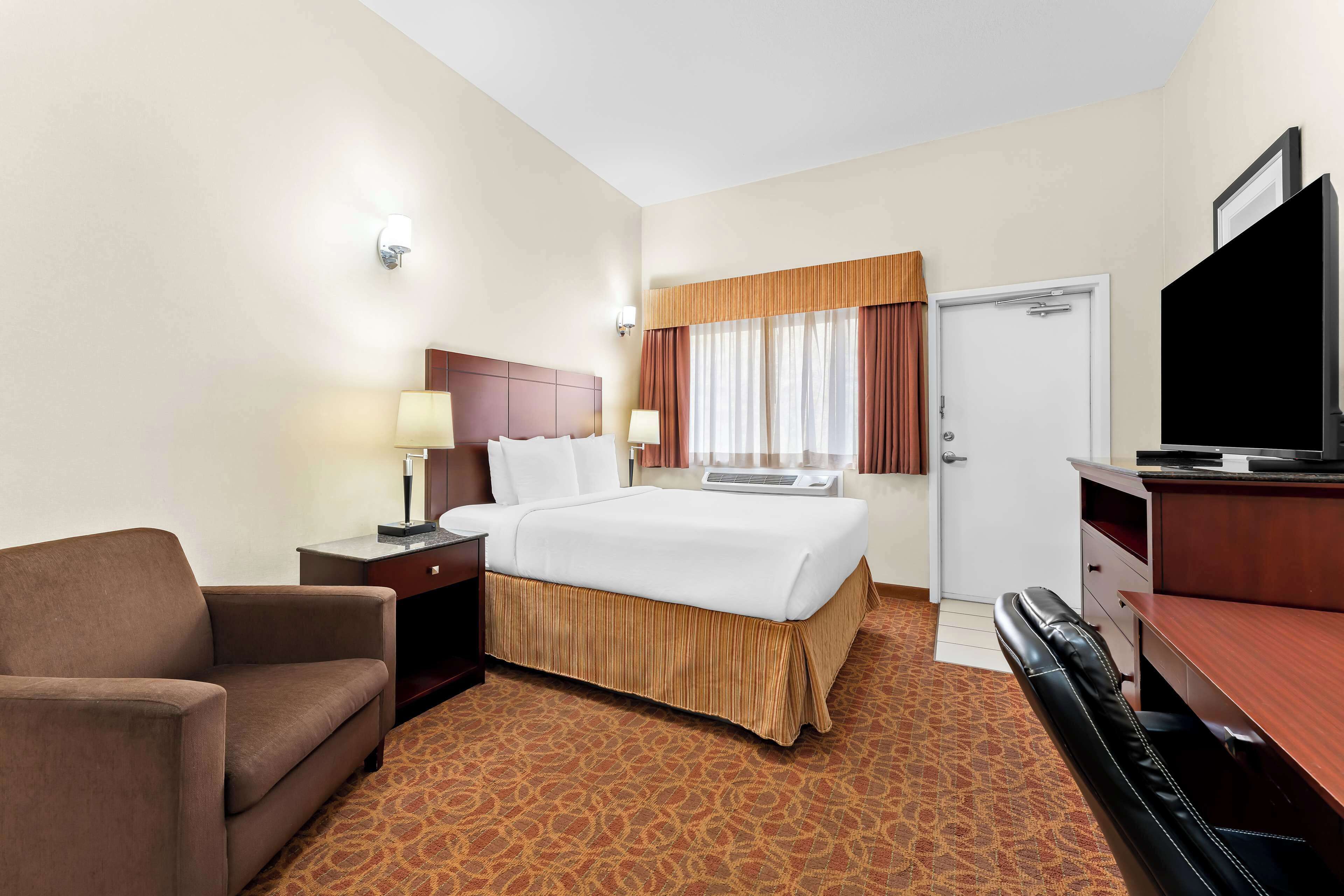 A hotel room with a bed, a desk, a chair, a television, and a door.