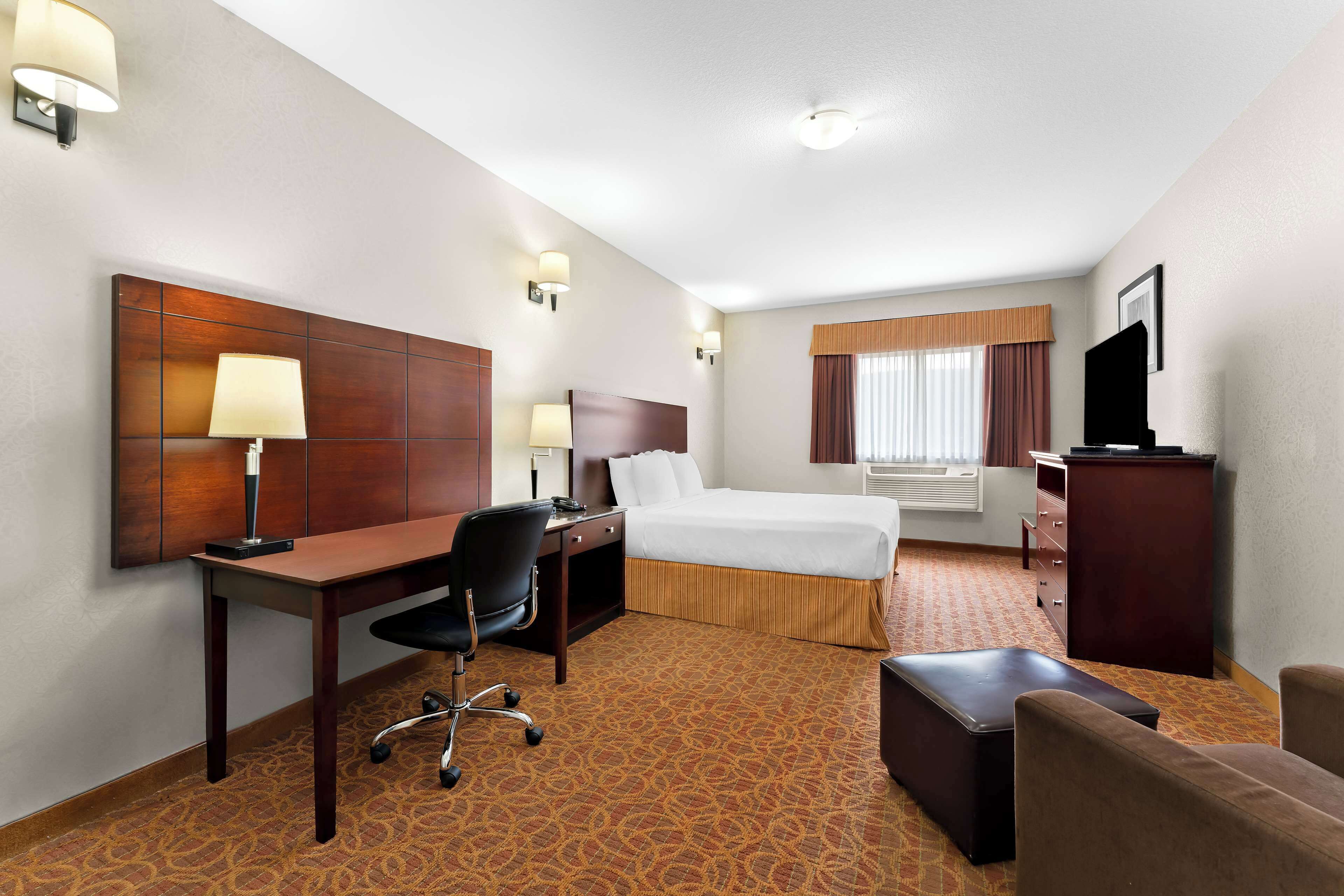 A hotel room with a bed, desk, chair, and a television.