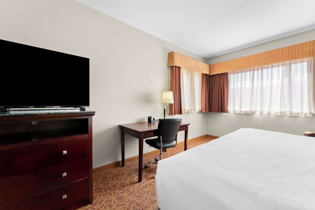 A hotel room with a bed, a desk with a chair, a television, and a window with curtains.