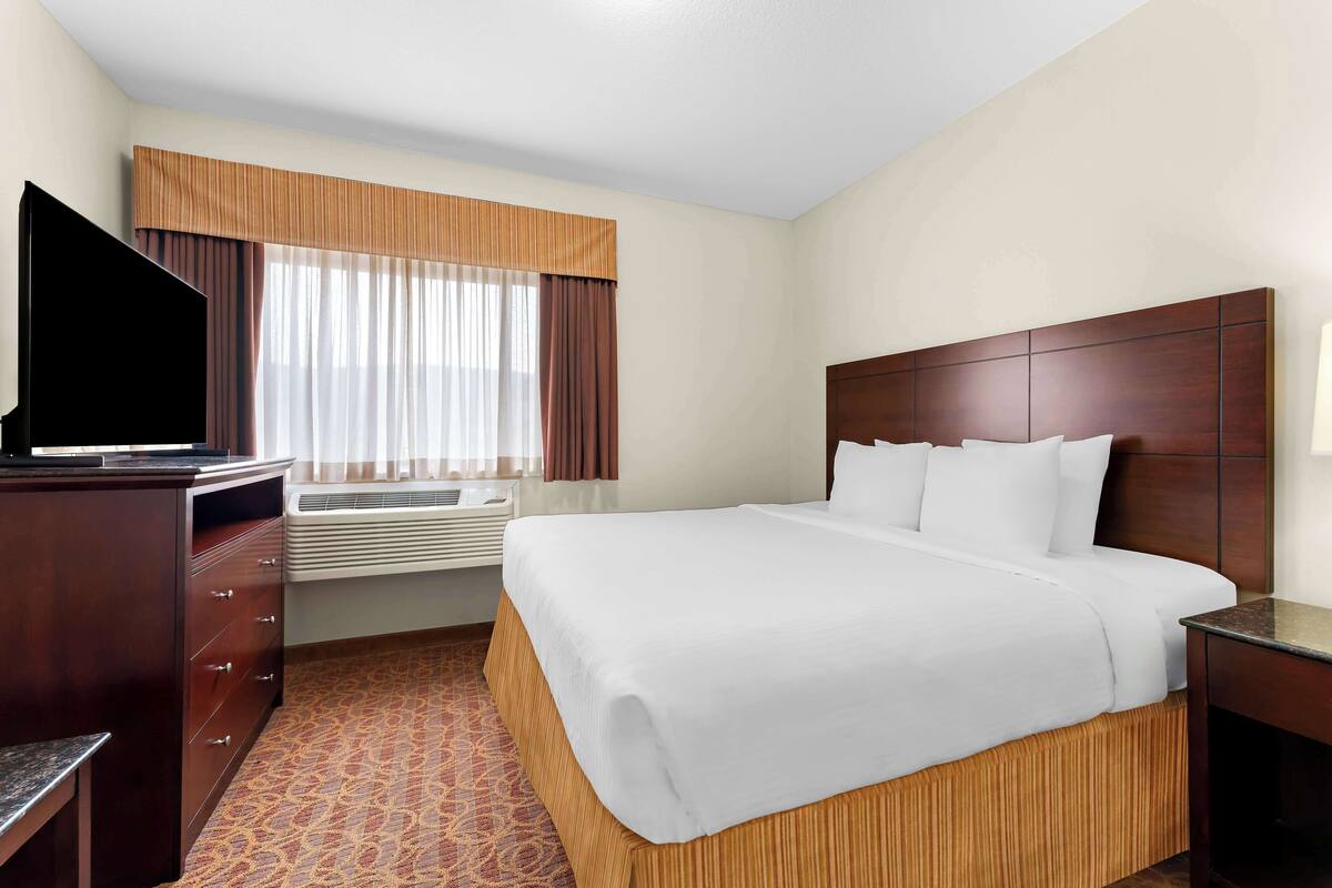 A hotel room with a large bed, a flat-screen TV, a dresser, and an air conditioning unit.