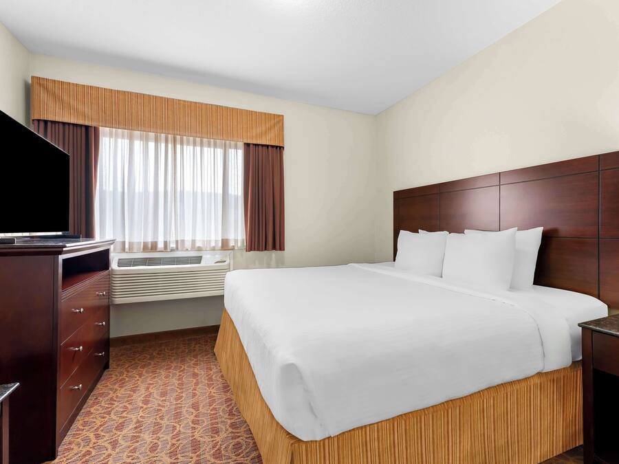 A hotel room with a large bed, a flat-screen TV, a dresser, and an air conditioning unit.
