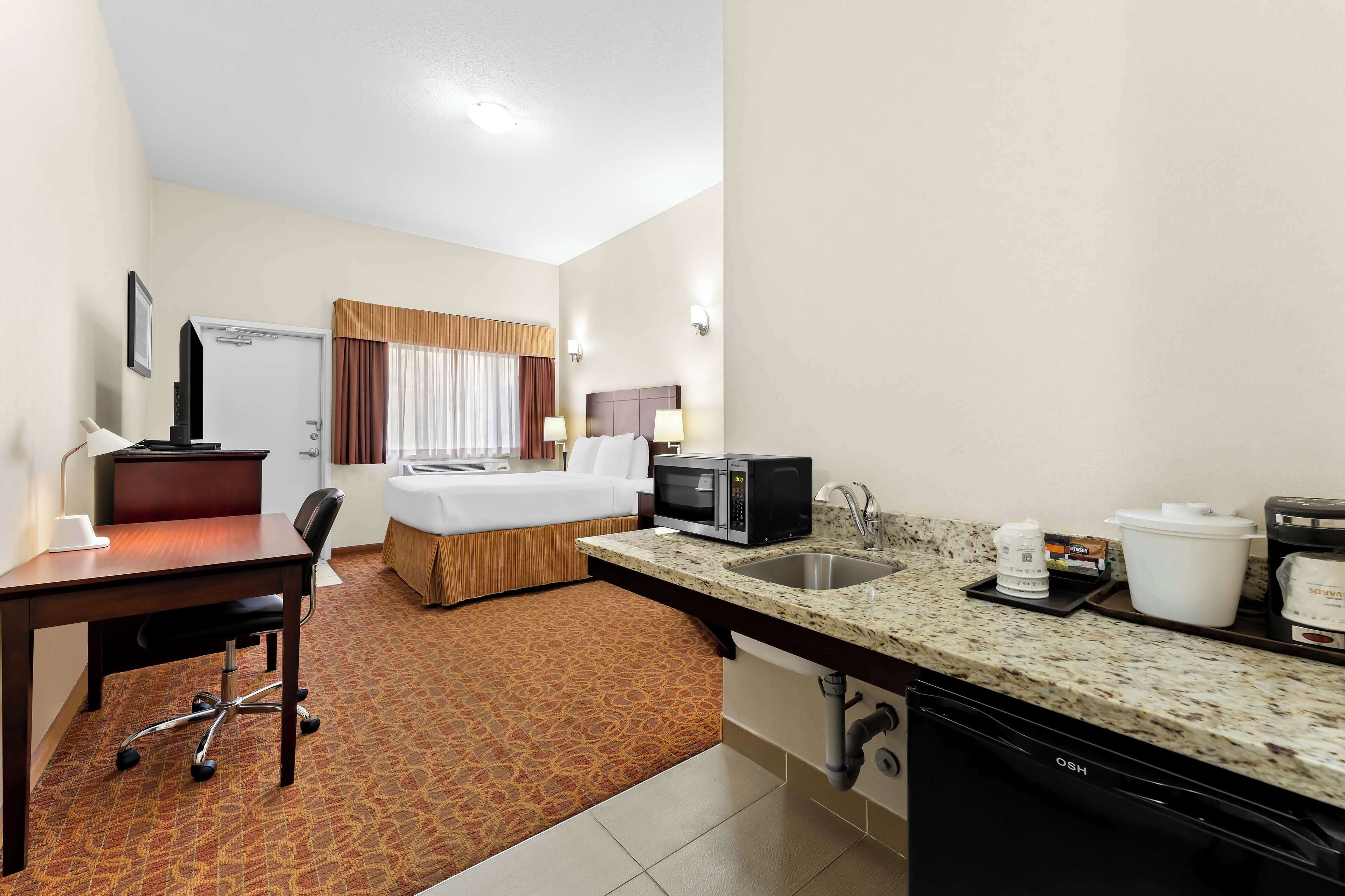 Quarto de hotel com cama, escrivaninha, micro-ondas, cafeteira e pia.