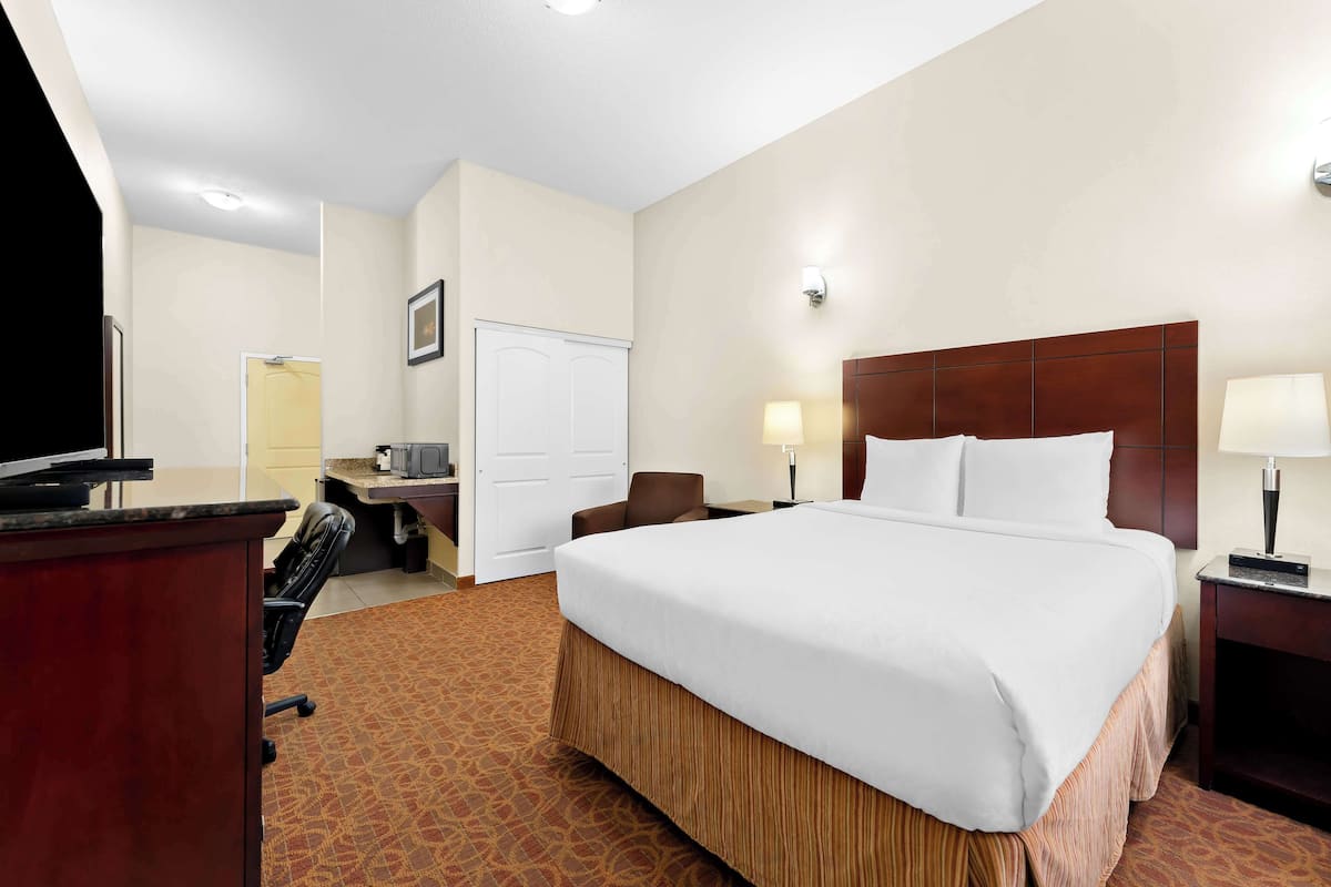 A hotel room with a large bed, a desk with a computer, a chair, and a television.