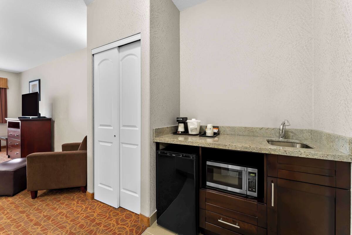 A compact hotel room with a kitchenette, including a microwave, coffee maker, and sink.