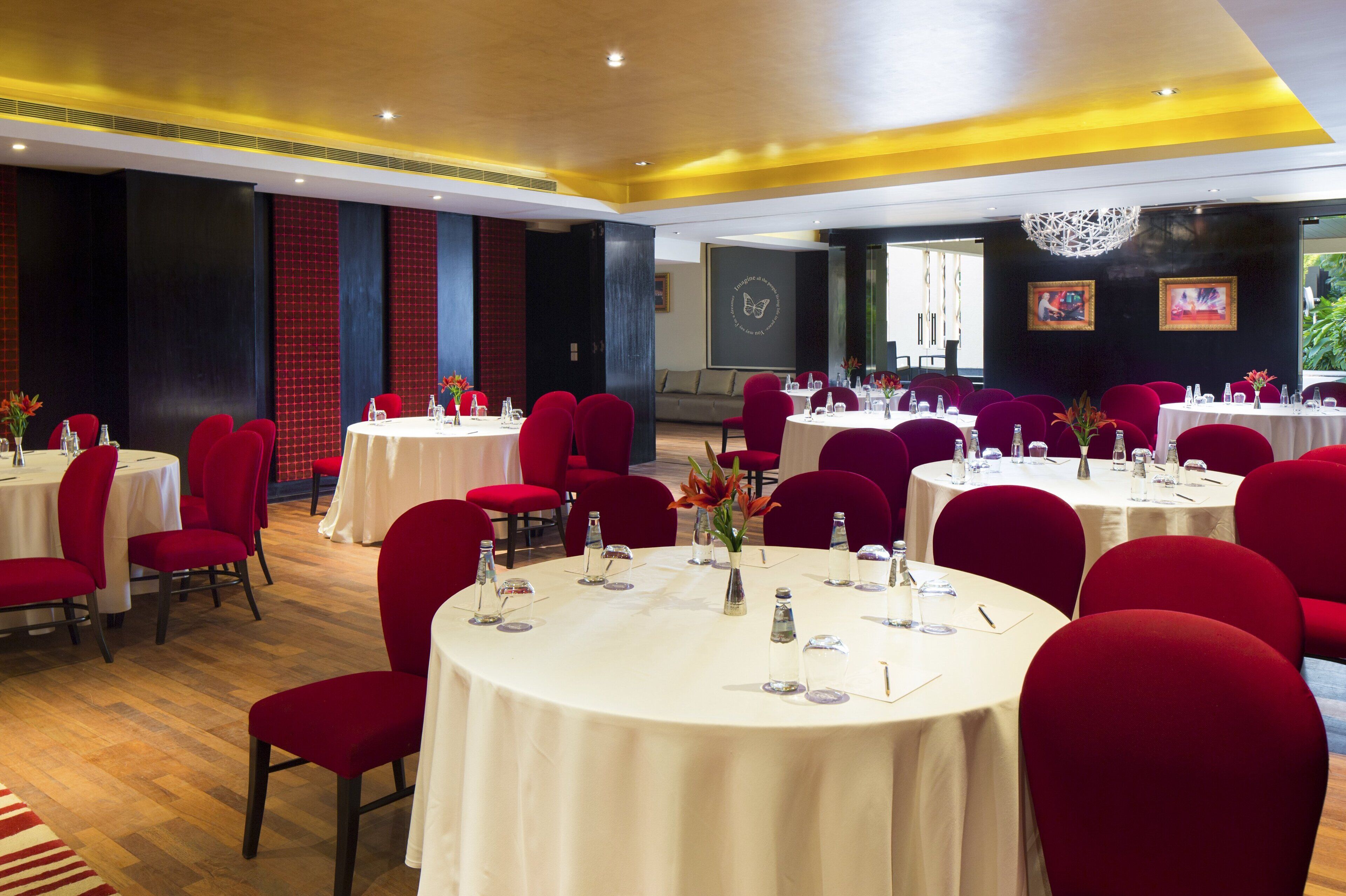 A conference room with round tables, red chairs, and white tablecloths.