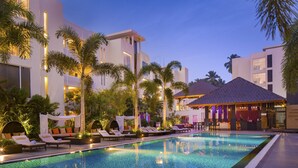 Una piscina con sillas de descanso y palmeras, rodeada de edificios modernos con balcones y una zona de bar.