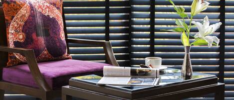 A room with a chair, a table, a magazine, a cup, and a vase with flowers.