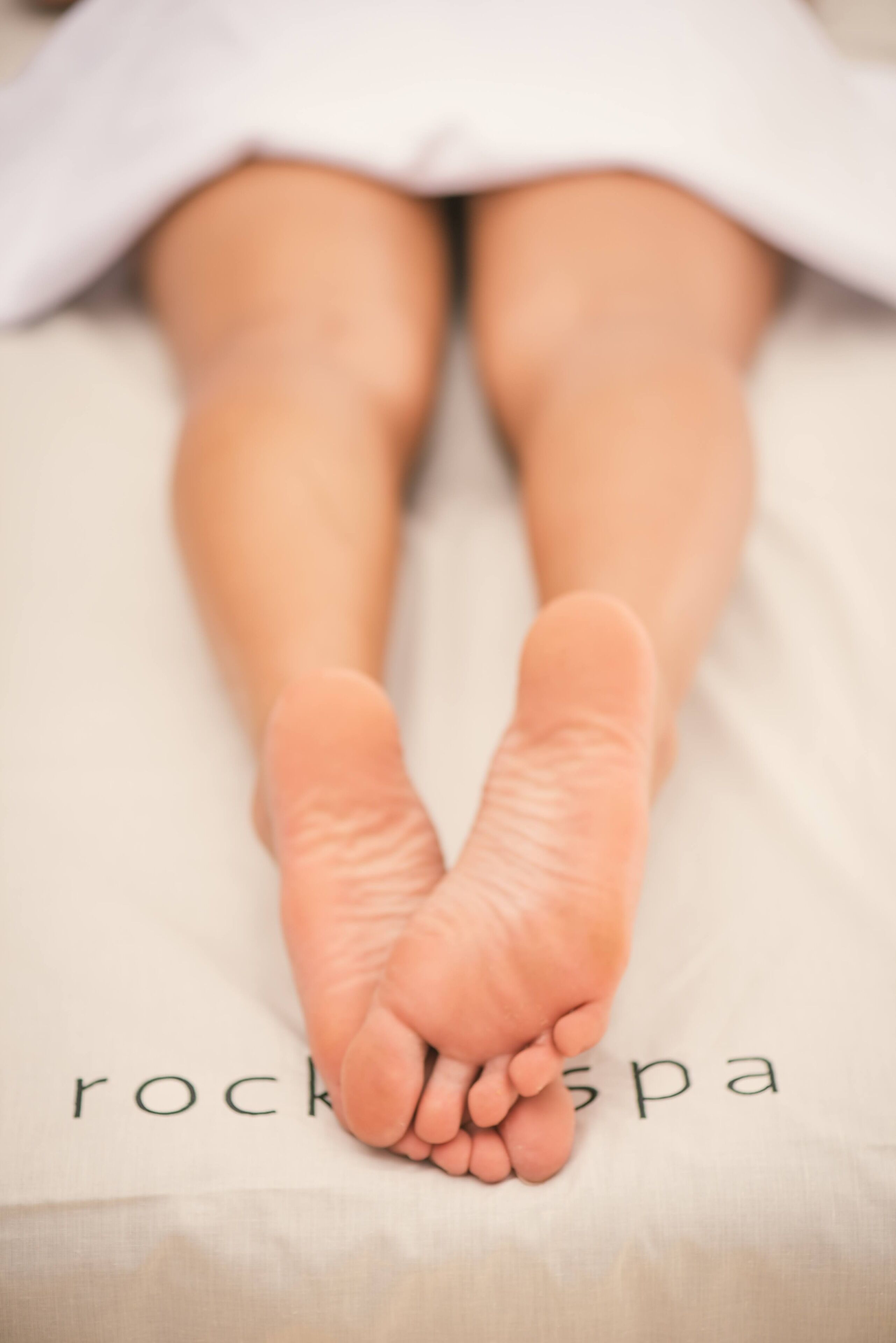 A close-up of a person's feet resting on a bed with the word "rockspa" visible on the bedspread.
