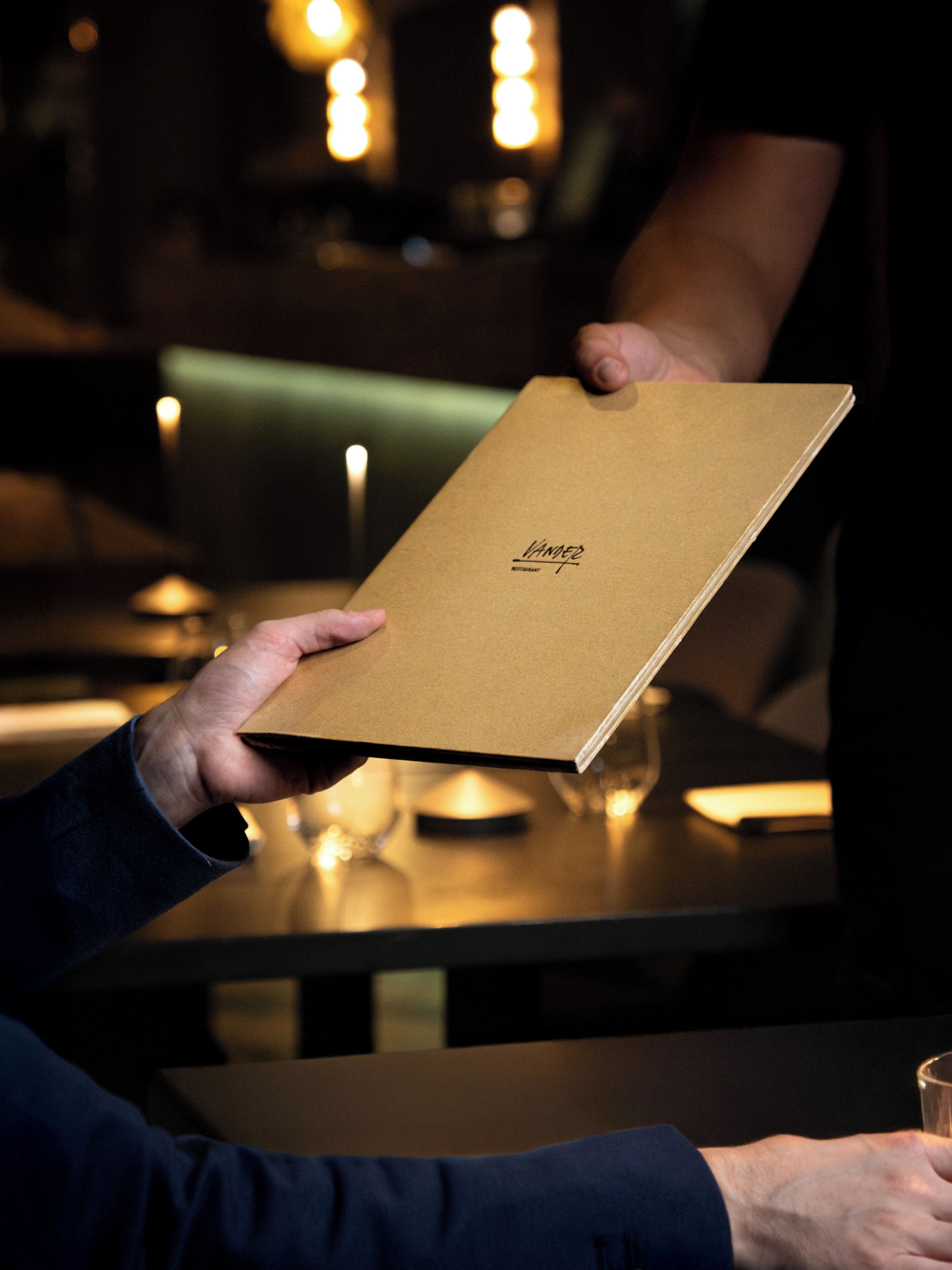 A person holding a brown menu with the text 'VAN DER ZANZ' on it.