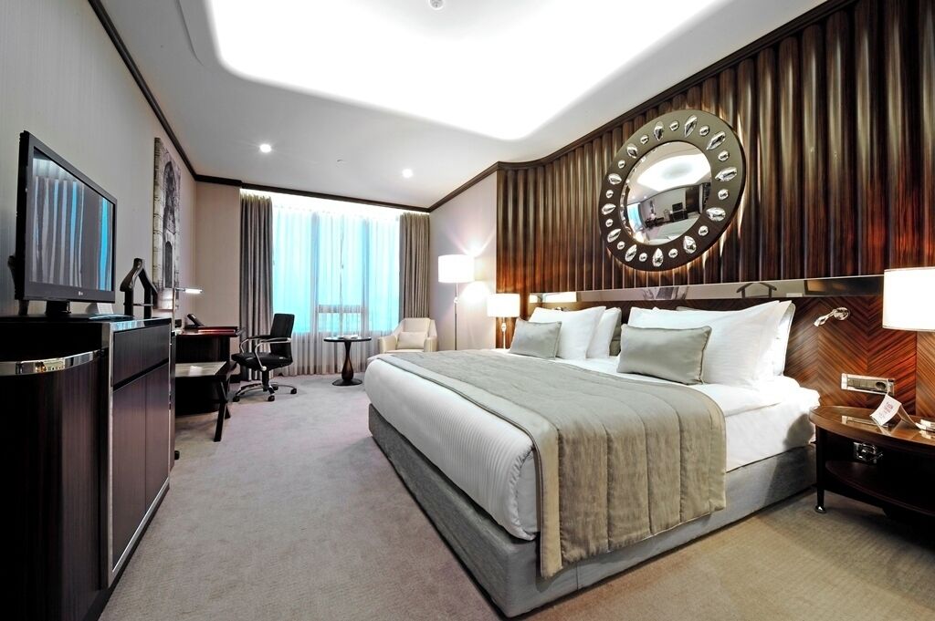 Une chambre d’hôtel avec un grand lit, un bureau avec un ordinateur, une télévision et un miroir au mur.