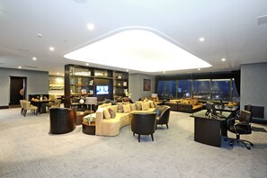 A spacious, modern lounge area with a curved sofa, a desk, and a large window offering a city view. - Crowne Plaza Bursa Convention Center & Thermal Spa by IHG (Bursa)