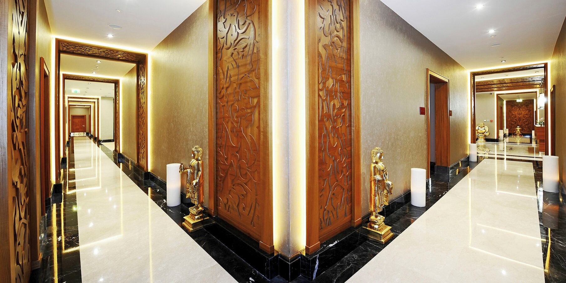 A luxurious hotel corridor with marble floors, ornate wooden paneling, and golden statues.