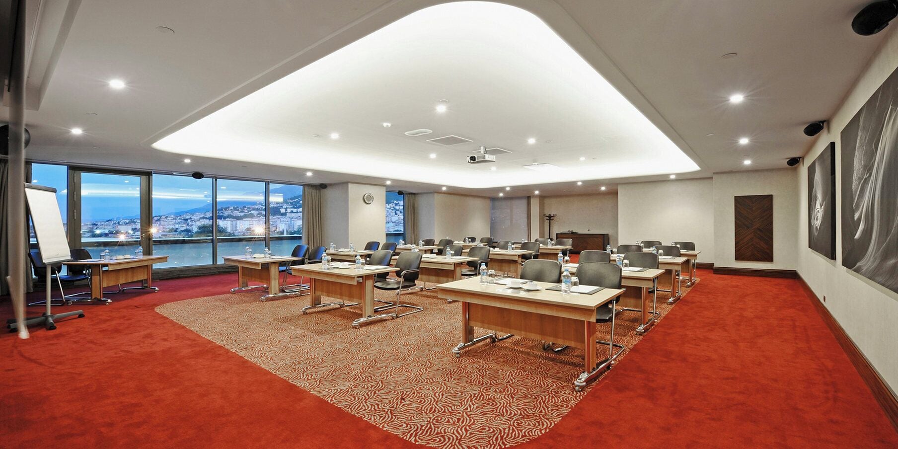 A conference room with multiple tables, chairs, and a large screen.