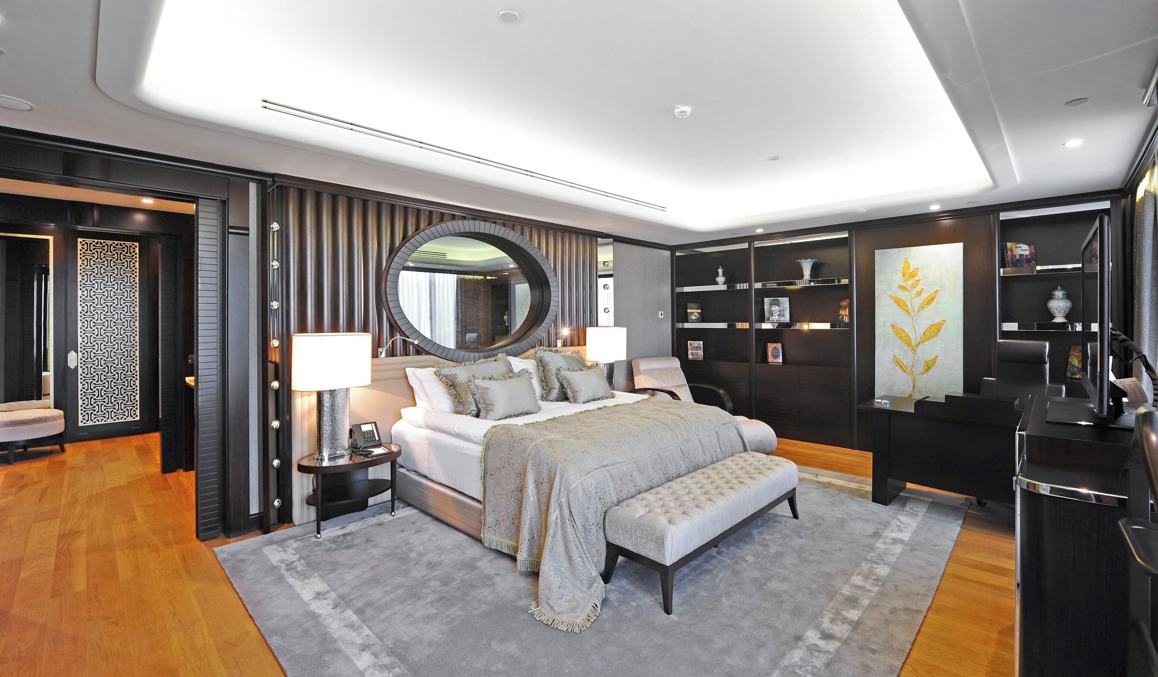 A modern bedroom with a large bed, bedside tables, a mirror, a desk, and a bookshelf.