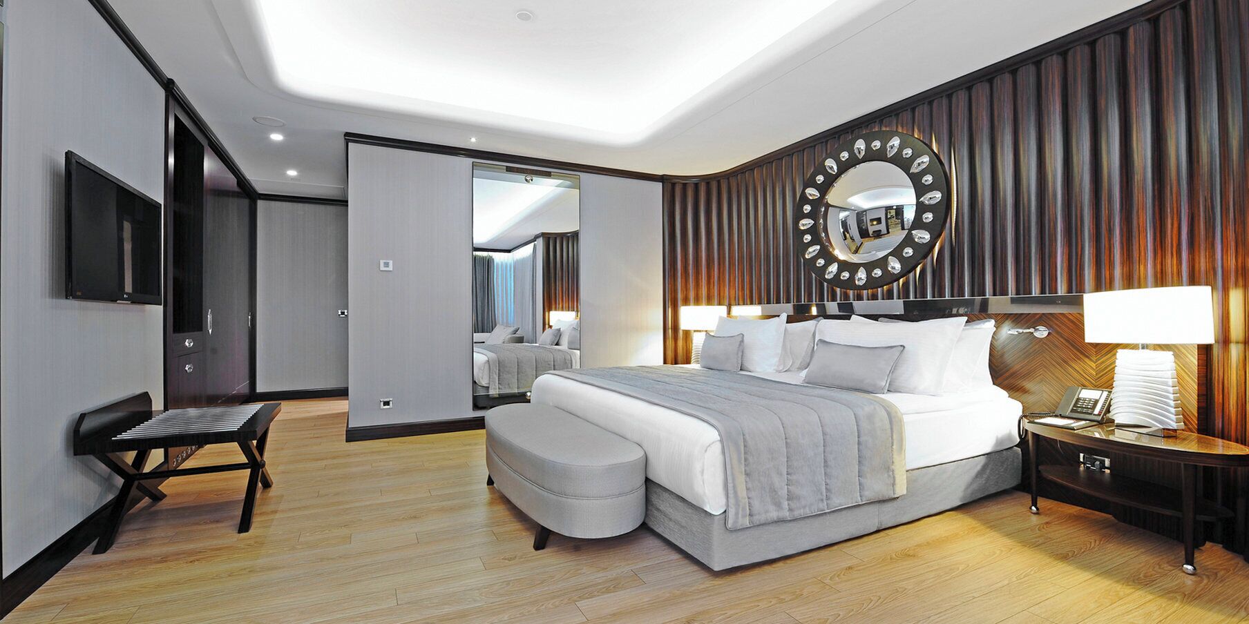 A modern hotel room with a large bed, bedside tables, a desk, and a mirror on the wall.