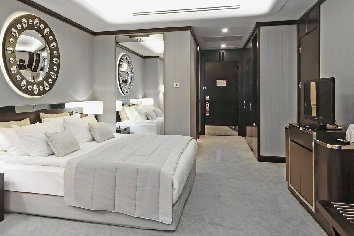 A hotel room with a large bed, bedside lamps, a desk with a telephone, and a television.