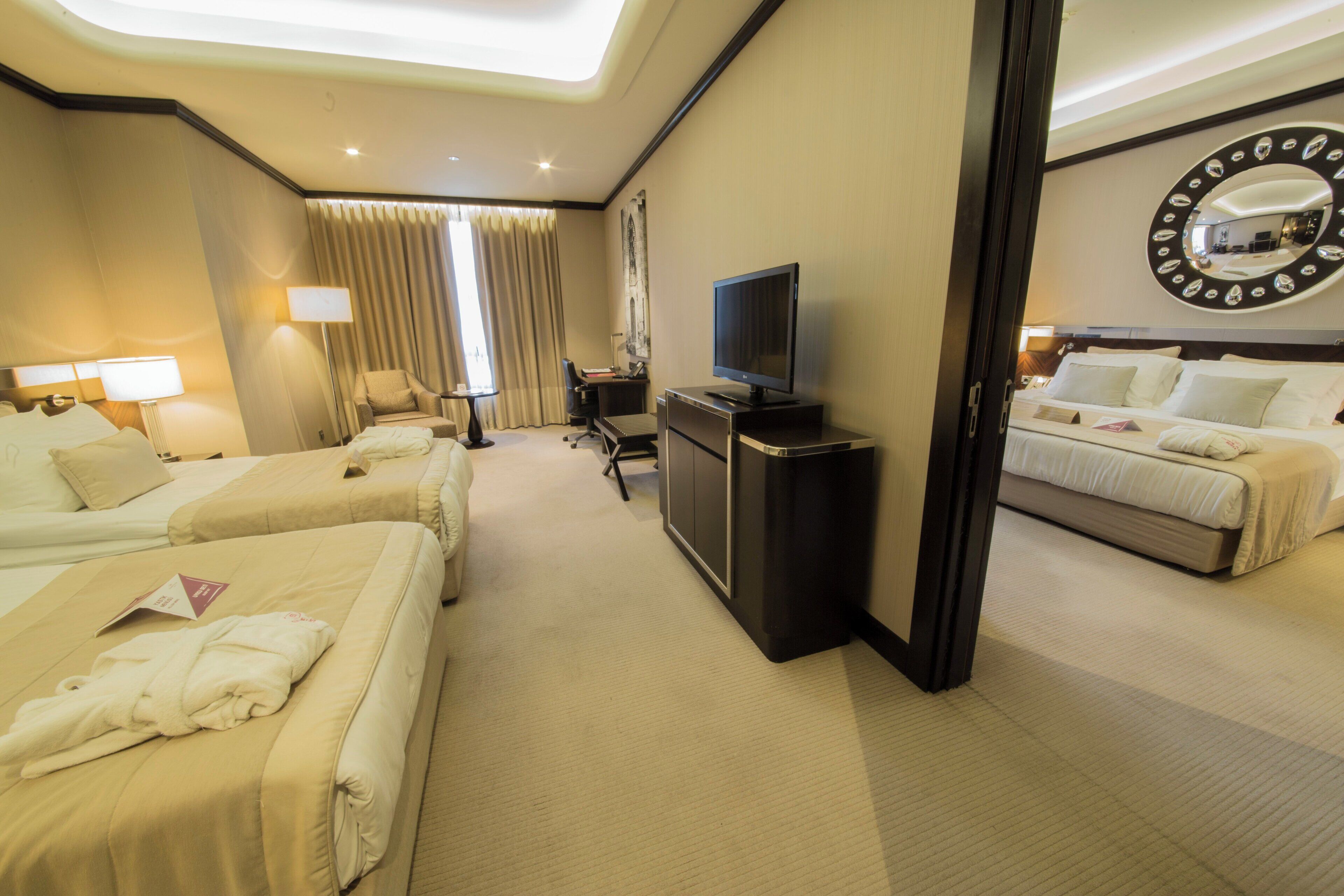 Habitación de hotel con dos camas, un escritorio, un televisor y un espejo grande.