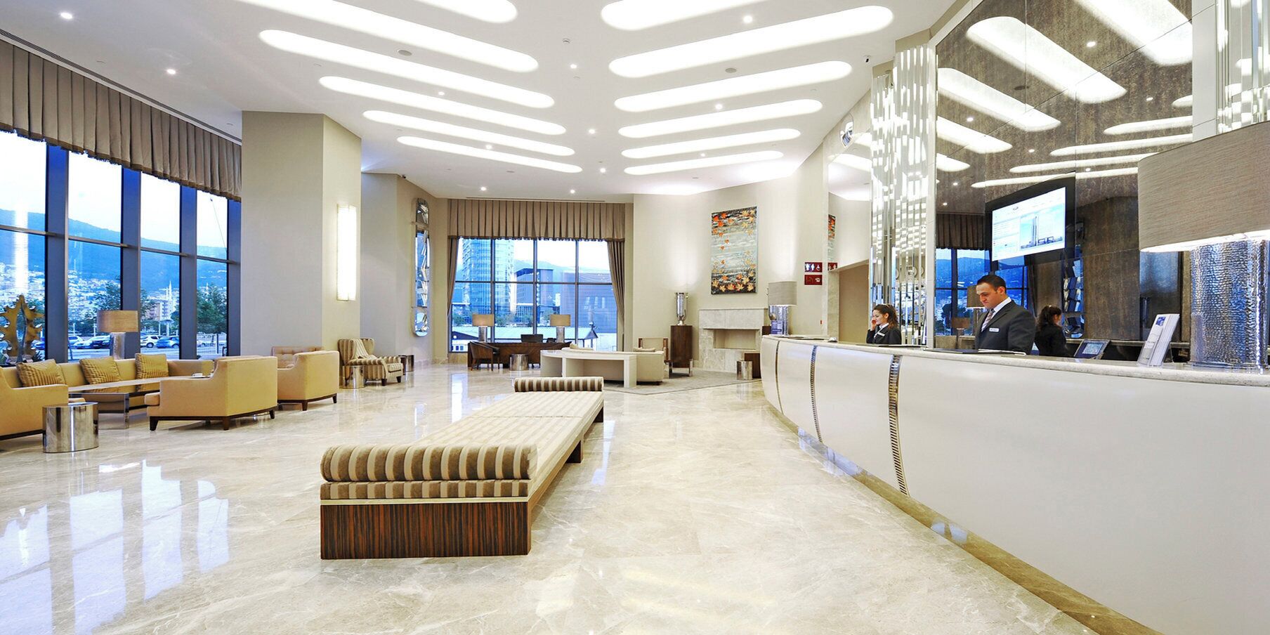 Un vestíbulo moderno de hotel con una recepción, zona de estar y grandes ventanales con vistas a la ciudad.