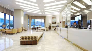 Un vestíbulo moderno de hotel con una recepción, zona de estar y grandes ventanales con vistas a la ciudad.