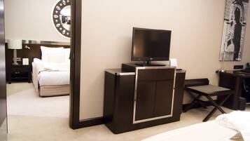 Une chambre d’hôtel comprenant un lit, un bureau avec un téléviseur à écran plat, une chaise, une lampe de bureau et une grande horloge murale.