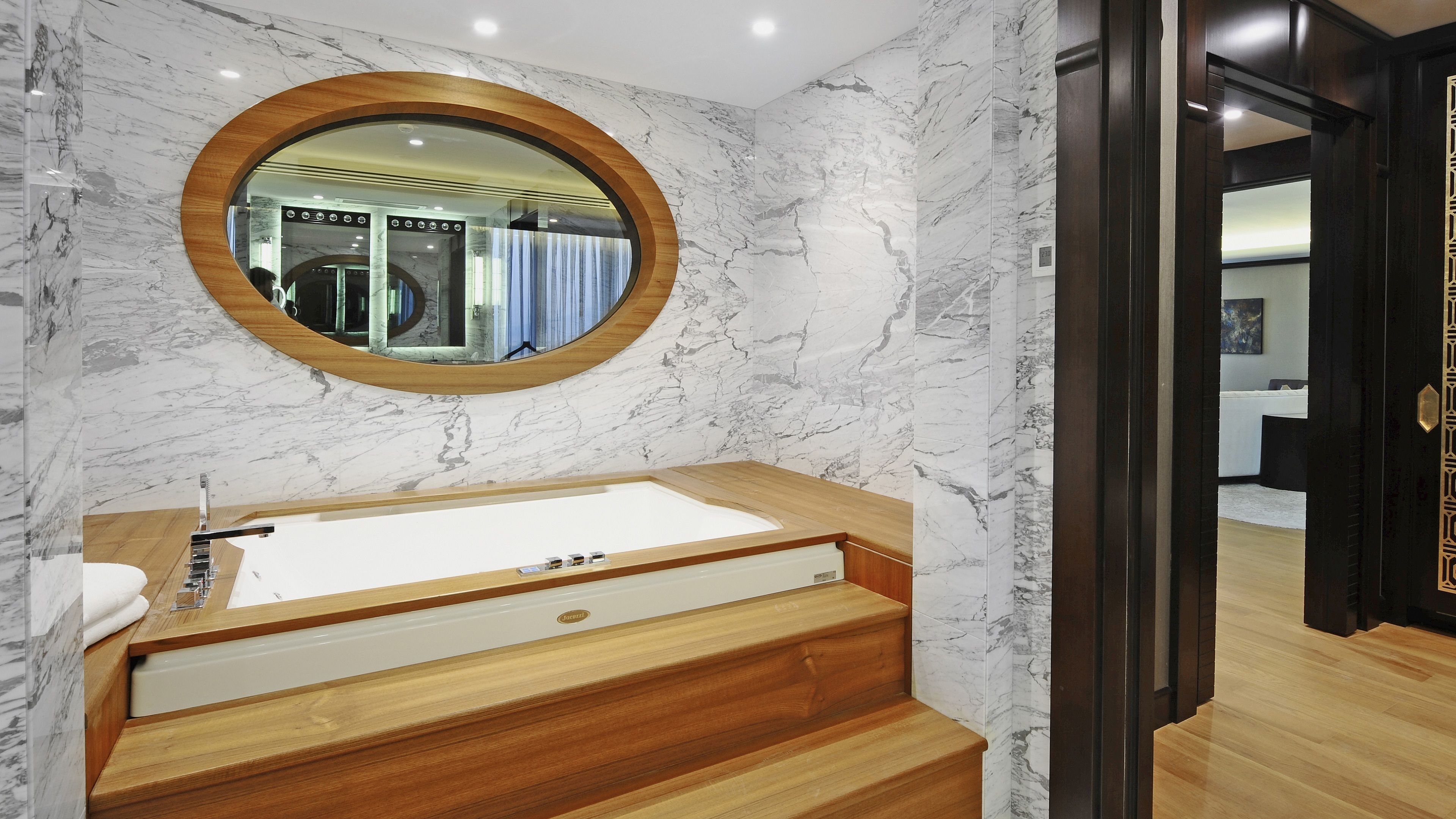 Un baño con pared de mármol, tocador de madera, un espejo grande y una bañera.