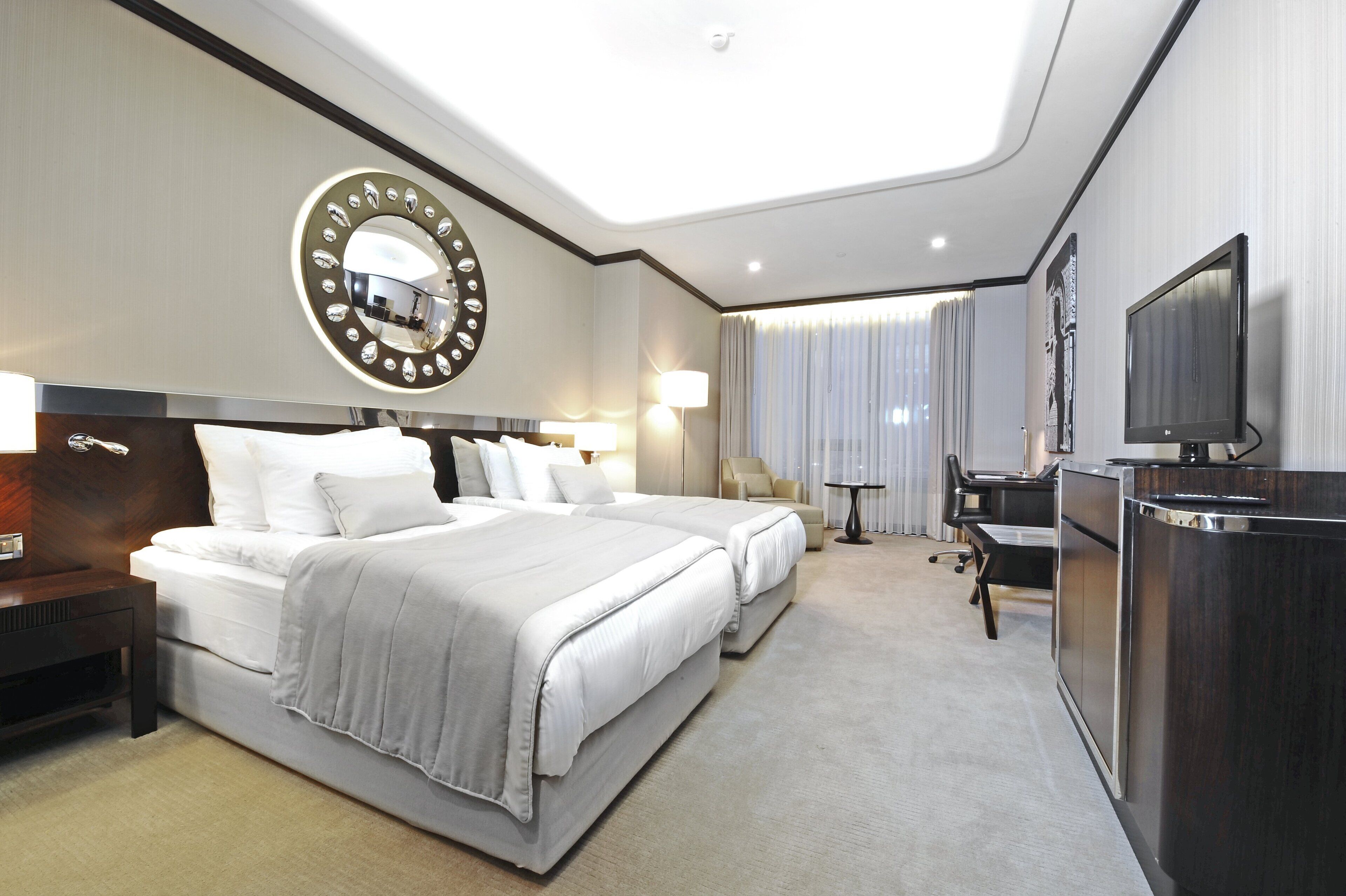 A hotel room with a large bed, a desk, a TV, and a mirror.