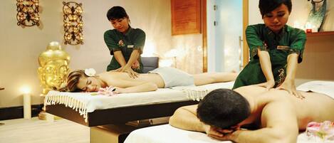 Un salón de terapia de masaje con dos clientes recibiendo tratamiento, un terapeuta atendiendo y una estatua de Buda al fondo.