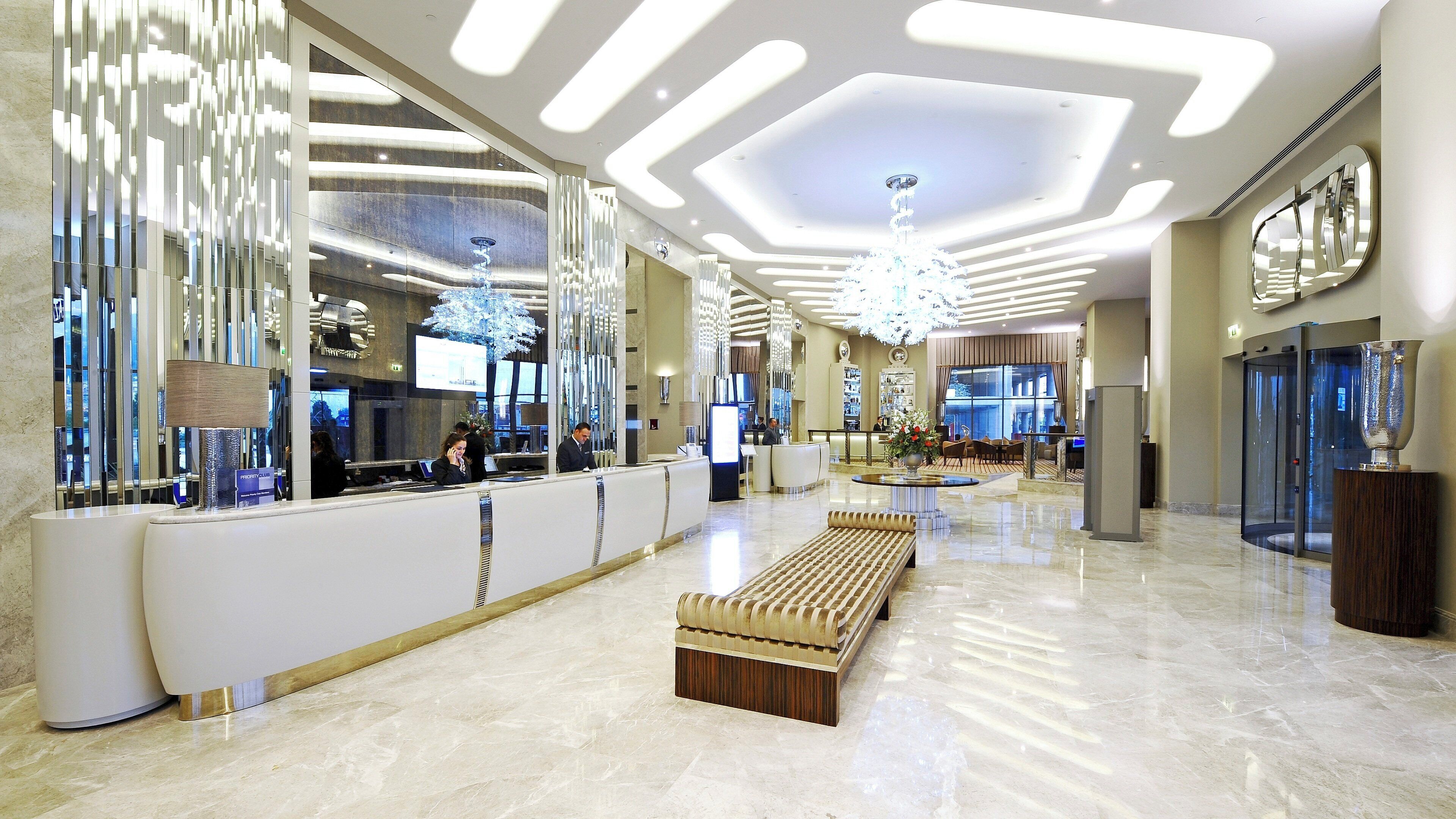 A modern lobby with a reception desk, seating area, and a large chandelier.