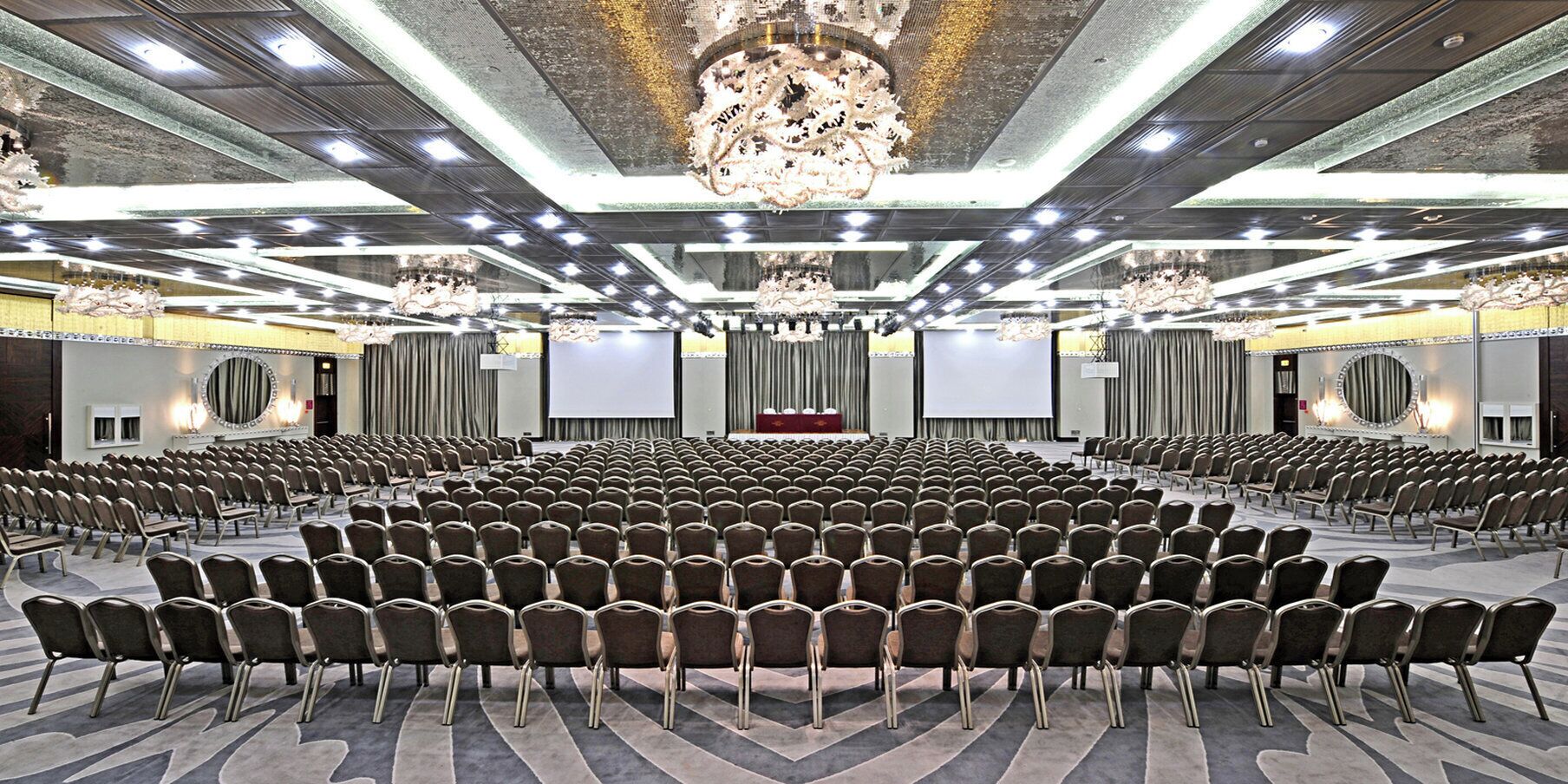 A large conference room with rows of chairs, a stage with a podium, and a large screen.