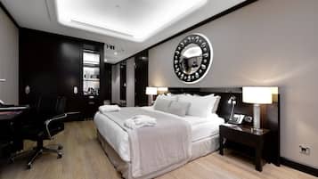 Una habitación de hotel moderna con una cama grande, un escritorio y una silla. Hay un espejo redondo en la pared y una mesita de noche con una lámpara.