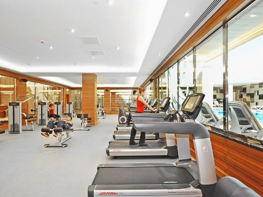 A modern gym with treadmills, weight machines, and a pool area visible through large windows.