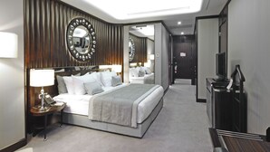 Una habitación de hotel moderna con una cama grande, una mesita de noche con lámpara, un espejo y un televisor.