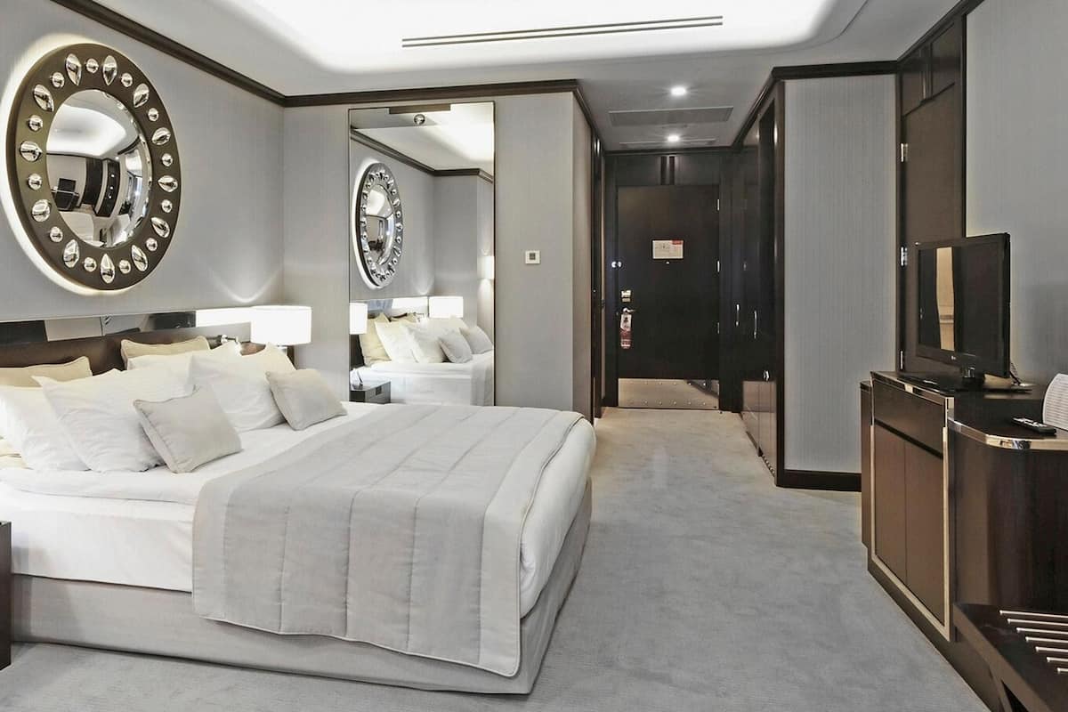 A hotel room with a large bed, bedside tables with lamps, a mirror, a desk with a television, and a wardrobe.