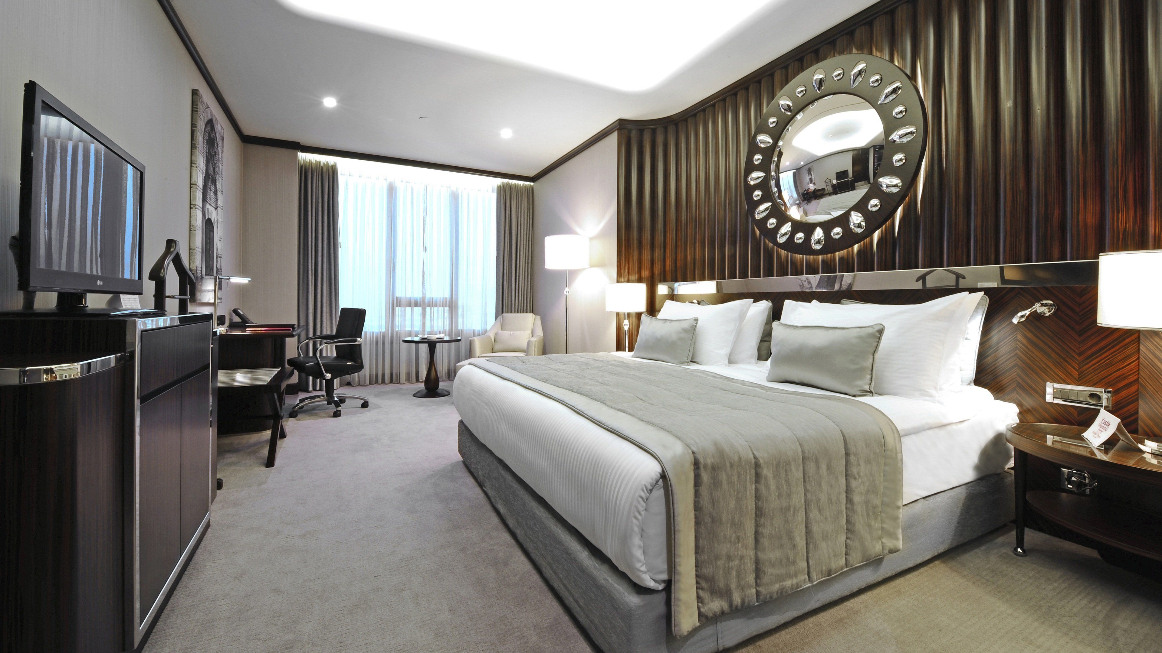 Habitación de hotel con una cama grande, un escritorio con computadora, una silla y un televisor.