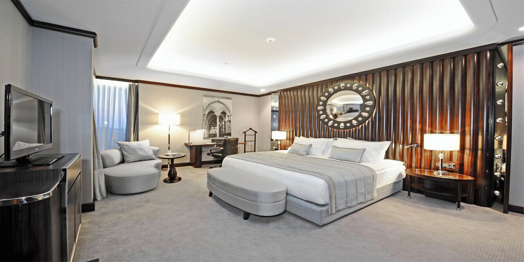 Una habitación de hotel con cama, televisión, escritorio, silla, lámpara y espejo.