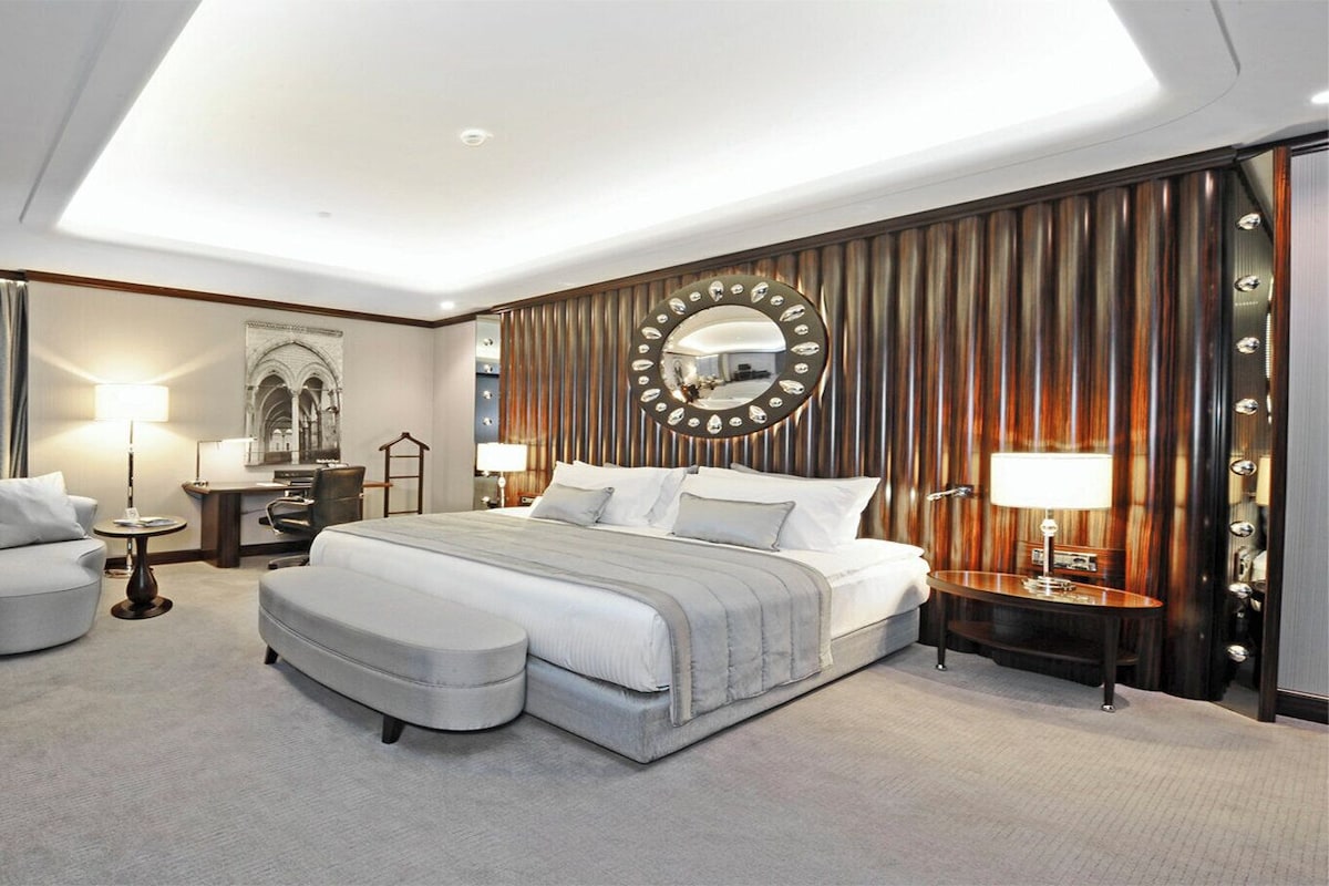 A hotel room with a bed, a TV, a desk, a chair, a lamp, and a mirror.