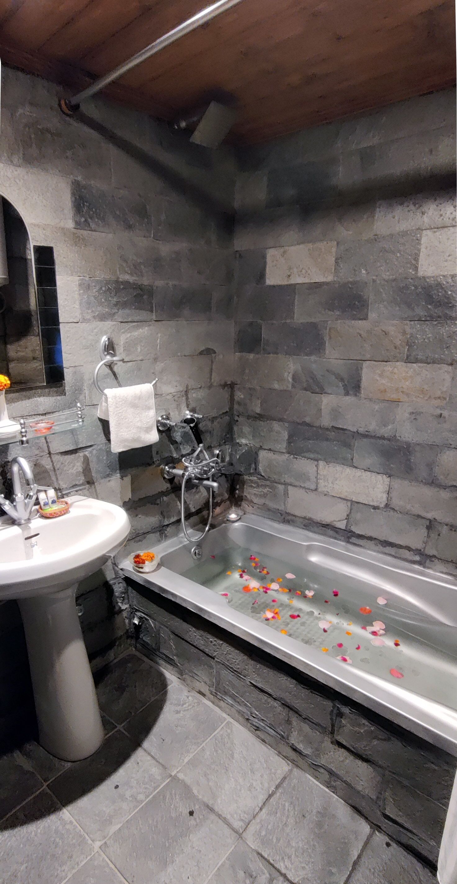 Une salle de bain avec un mur en pierre, un lavabo, une baignoire et une douche.