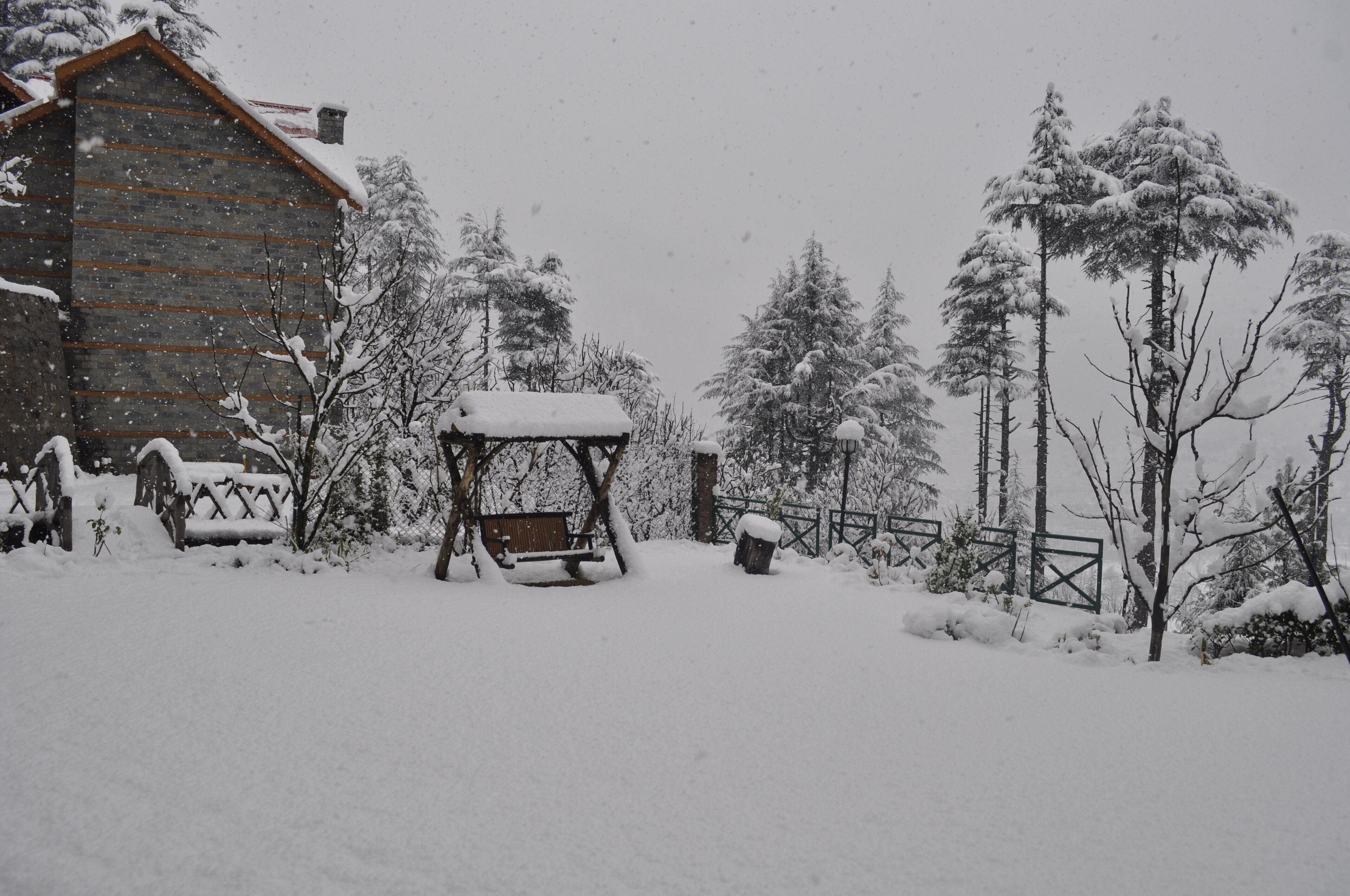 Una cabaña de madera con tejado nevado, rodeada de árboles cubiertos de nieve y una valla de madera.