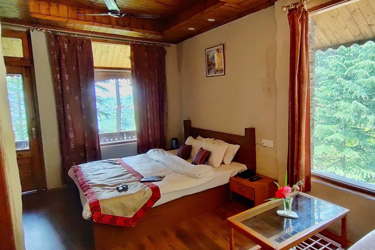 Une chambre à coucher avec un lit, une table de chevet et une fenêtre donnant sur des arbres.