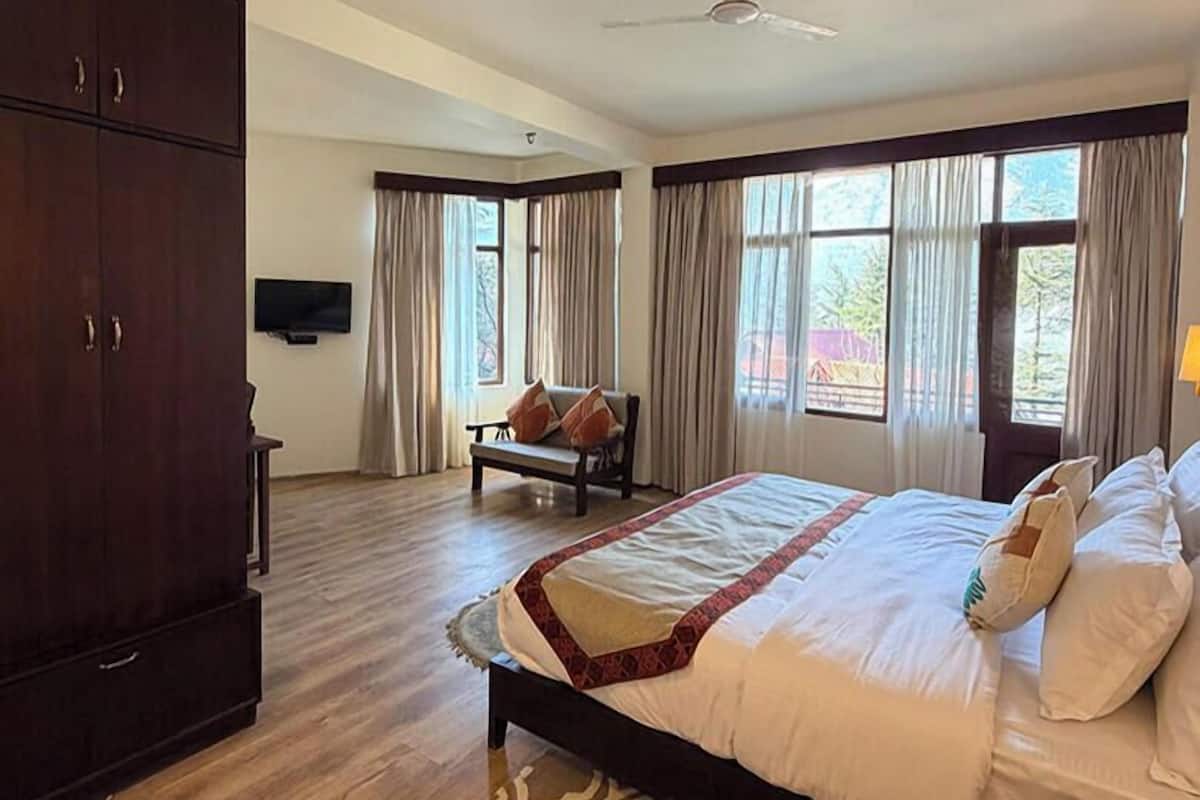 Une chambre d’hôtel équipée d’un lit, d’une armoire, d’un canapé, d’une télévision et de grandes fenêtres avec des rideaux.