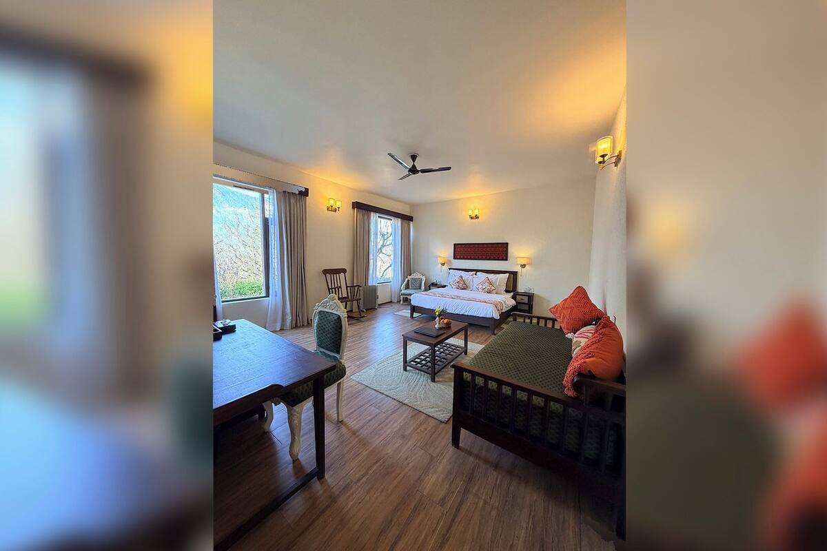Une chambre d’hôtel avec un lit, un bureau, une chaise, un ventilateur de plafond et une fenêtre.