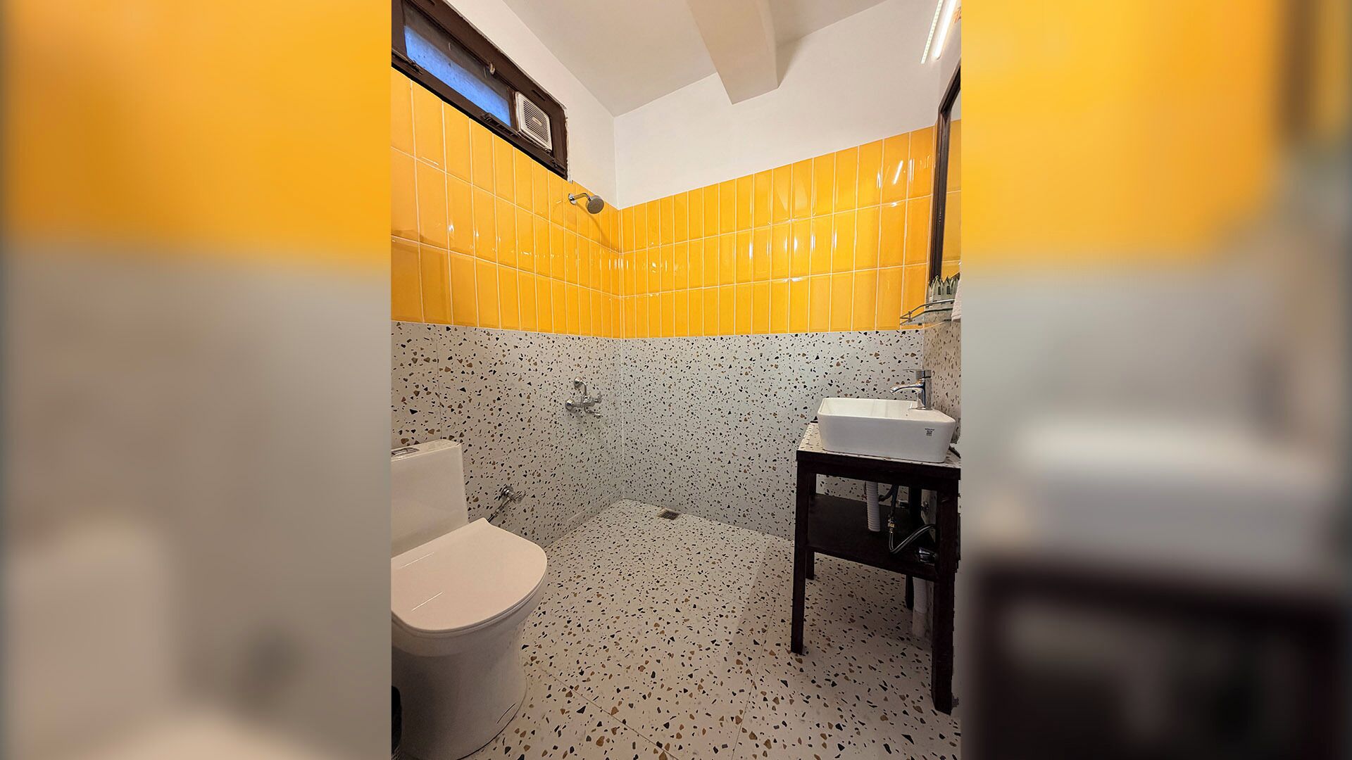 A bathroom with a toilet, sink, and shower. The walls are tiled in yellow and white.